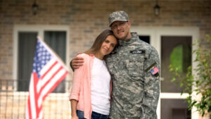 VA Home Loans former soldier and girlfriend hugging, standing against usa flag, homecoming